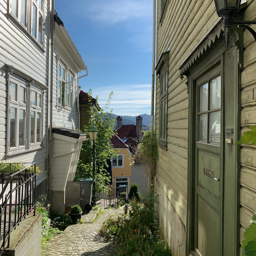 Trång trähusgränd med massa grönska emellan, i Bergen i Norge