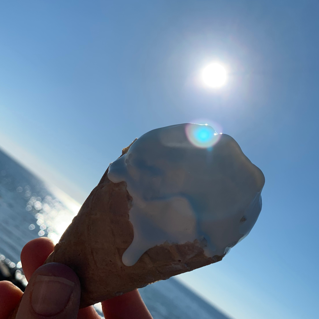 En rinnande glasstrut i motljus med en blå horisont och ett glittrande hav i nakfrunden, i Varberg
