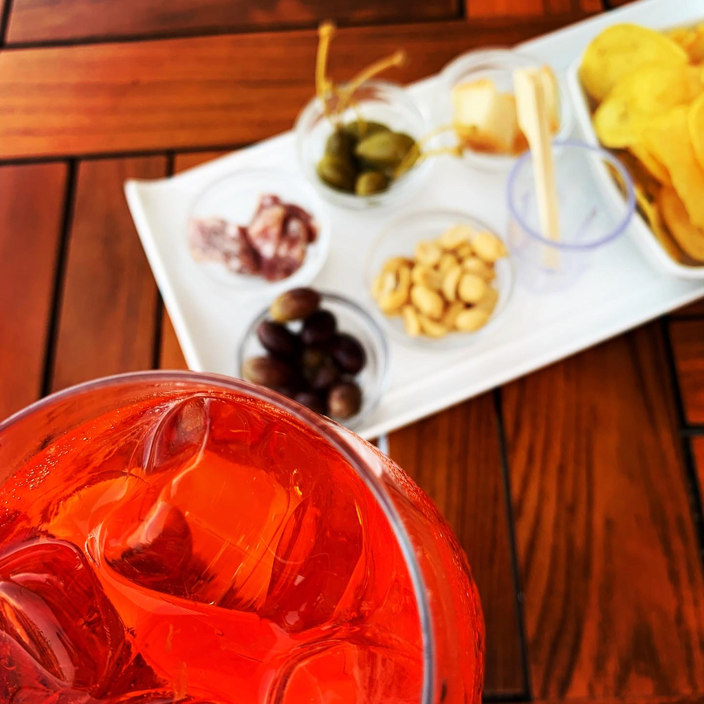 Ett glas aperil spritz med aperitivo bestående av oliver, nötter, kapris, ost, salami och chips