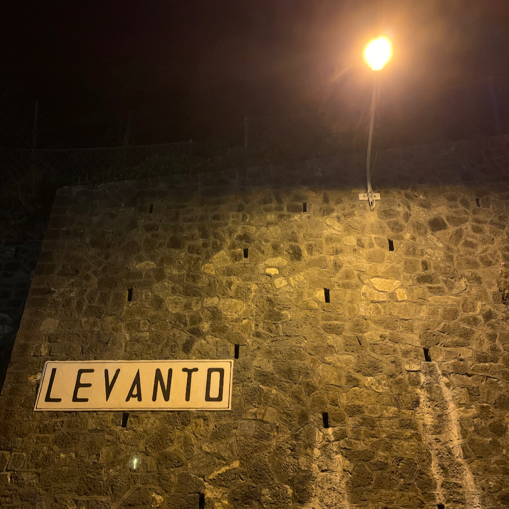 En gatlampa och stationsskylt i kvällsmörker som det står Levanto på i Cinque Terre Italien