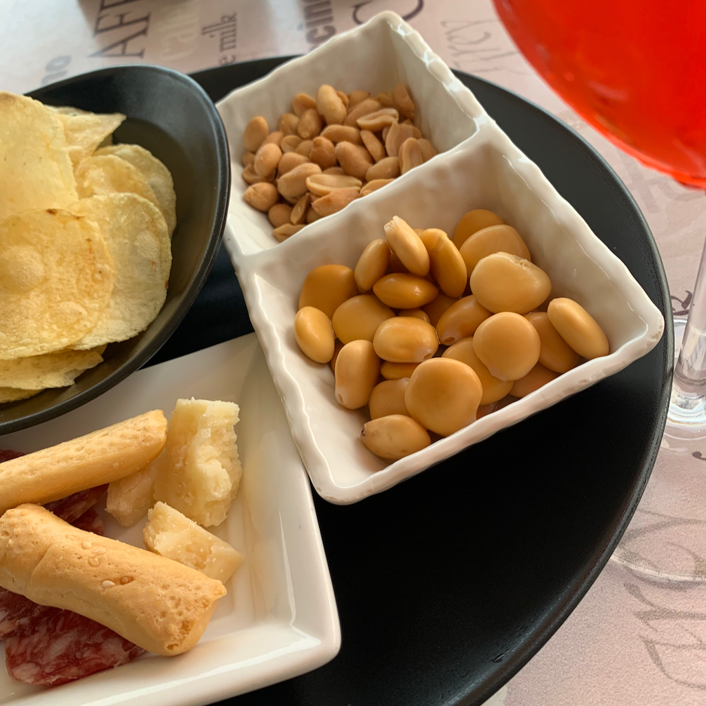 Ett glas aperol spritz och aperitivo bestående av chips, parmesanost, salami, krutonger, nötter och rostade vita bönor