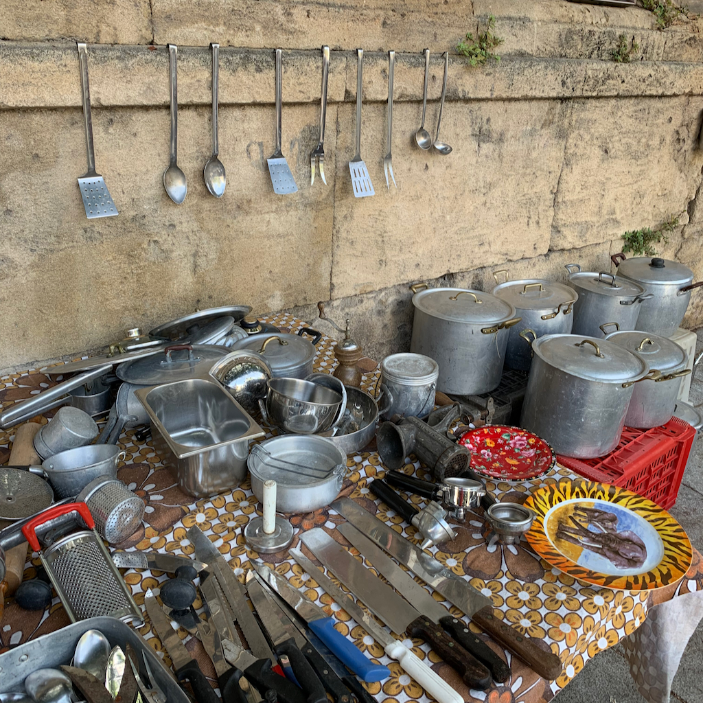 Ett bord med gamla kökkärl och tavlor på en söndagsloppis i Palermo på Sicilien i Italien