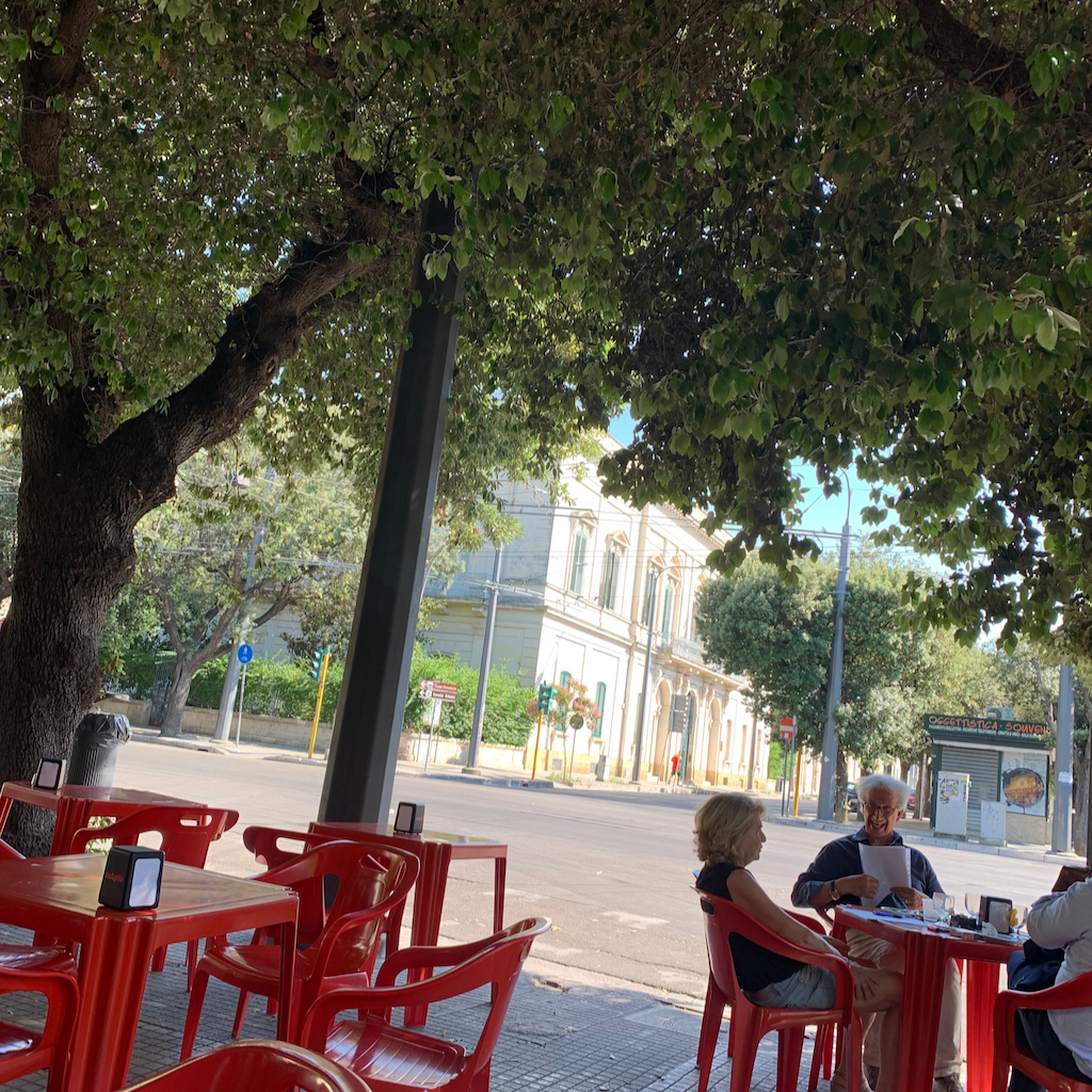 Ett barcafé med röda bord och plaststolar i en trafikerad gatukorsning i Lecce Italien
