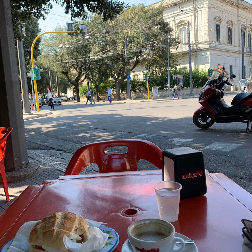 Ett genuint barcafé med röda bord och plaststolar i en trafikerad gatukorsning i Lecce Italien