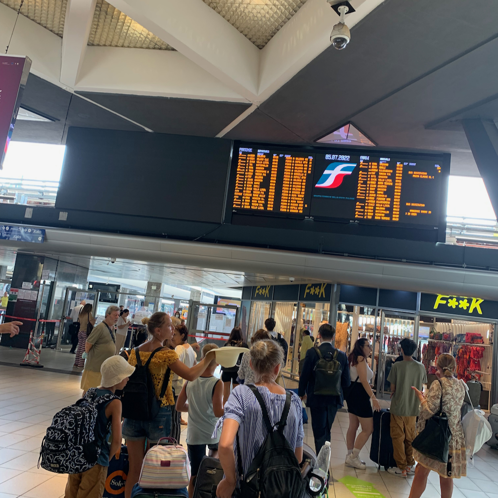 Människor står och tittat på tavlan för avgångstider på tågstationen i Napoli i Italien