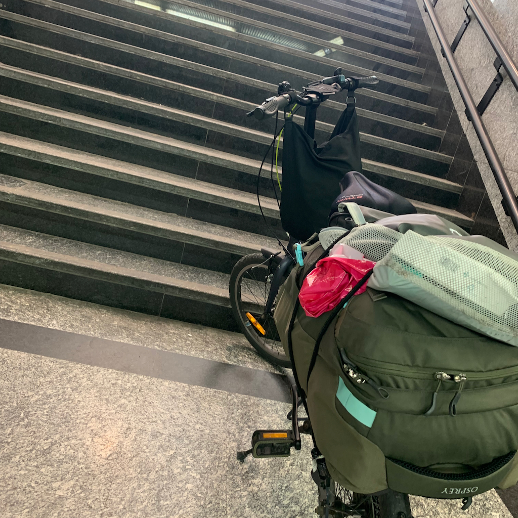 En fällbar cykel fullastad med packning vid en trappa på en tågstation i Italien