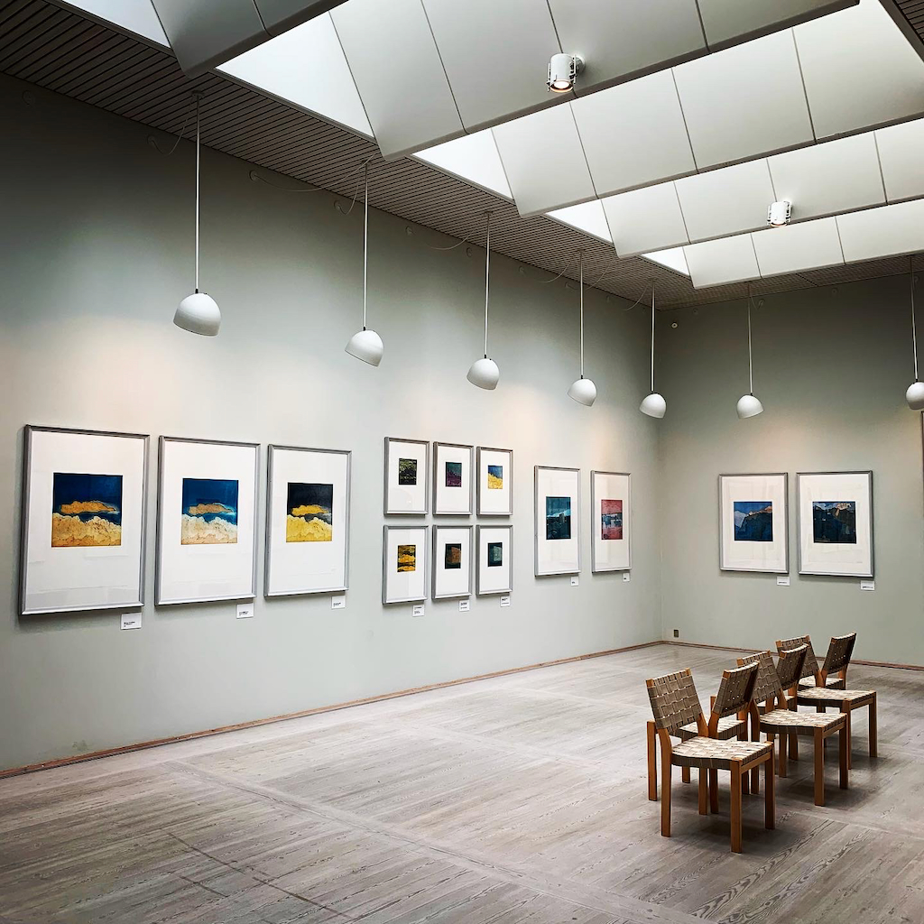 En utställningssal med takljusinsläpp, runda takpendyler och trästolar på Bornholm Kunstmuseum i Danmark