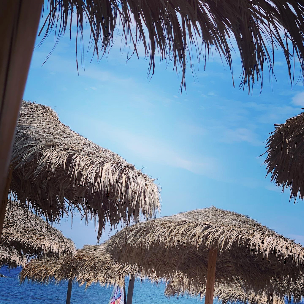 Solparasoller av palmblad på Kamari Beach på Santorini i Grekland