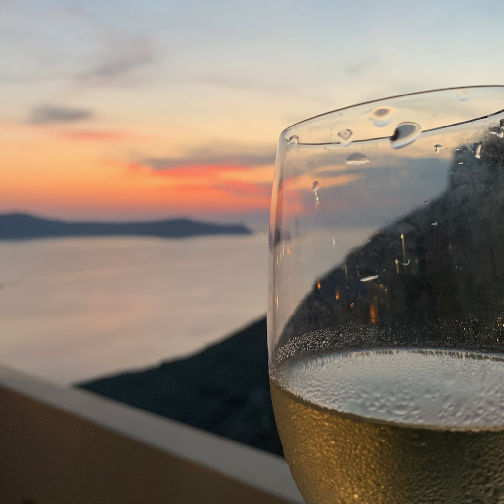 Ett glas vitt assyrtikovin i solnedgången i Oia på Santorini i Grekland