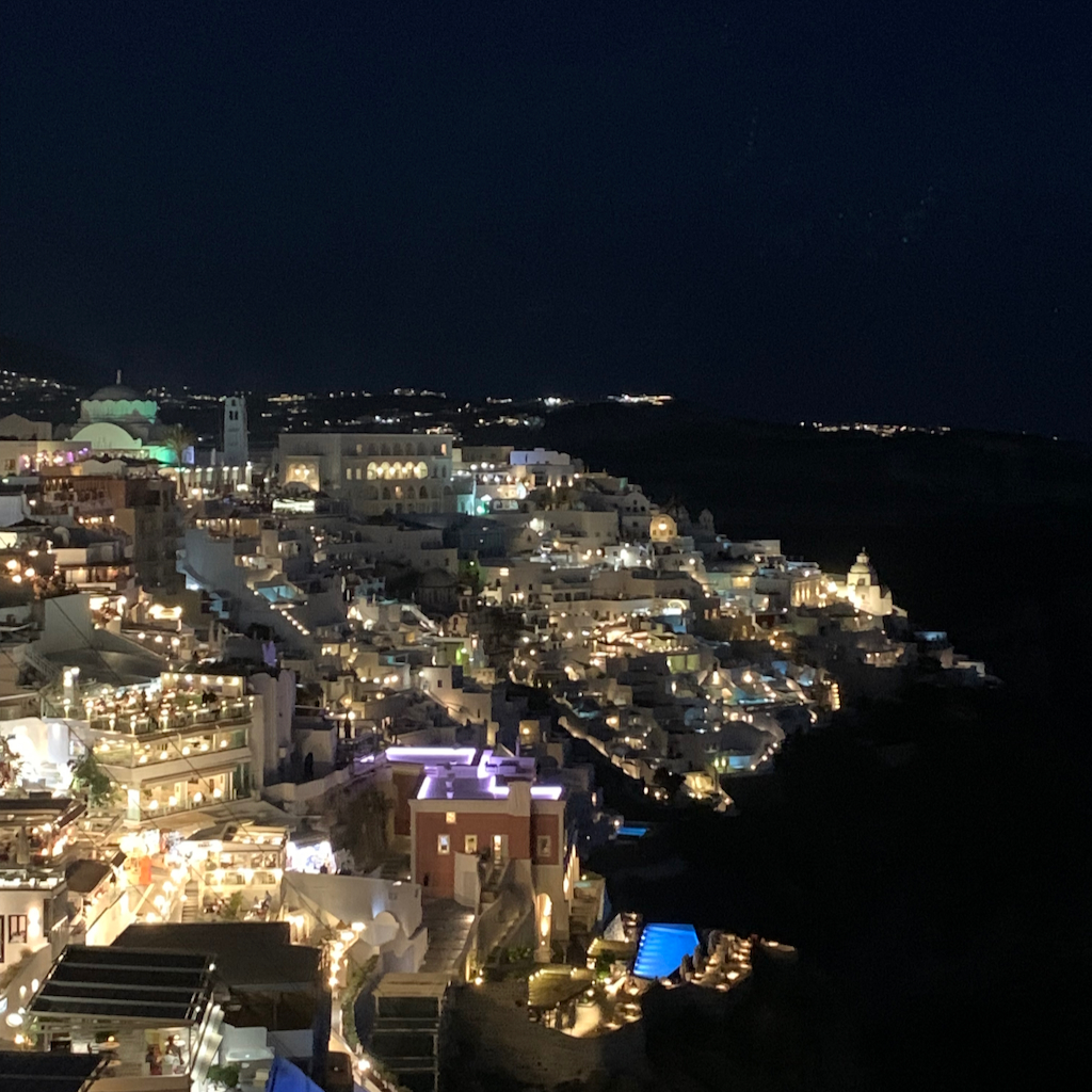 En nattbild av den upplysta turisthålan Oia på Santorini i Grekland