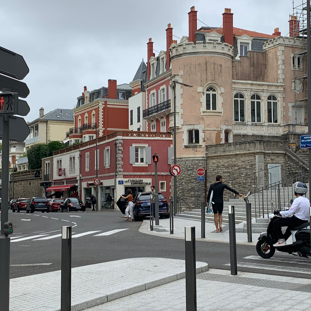 En gatukorsning i Biarritz i Frankrike där en man med surfingbräda under armen korsar gatan
