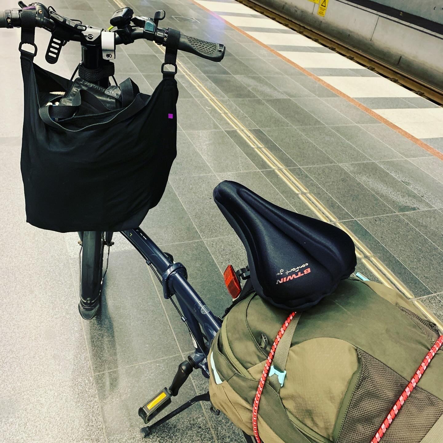 En fällbar cykel med en Osprey ryggsäck fastspänd på pakethållaren på en tågperrong.
