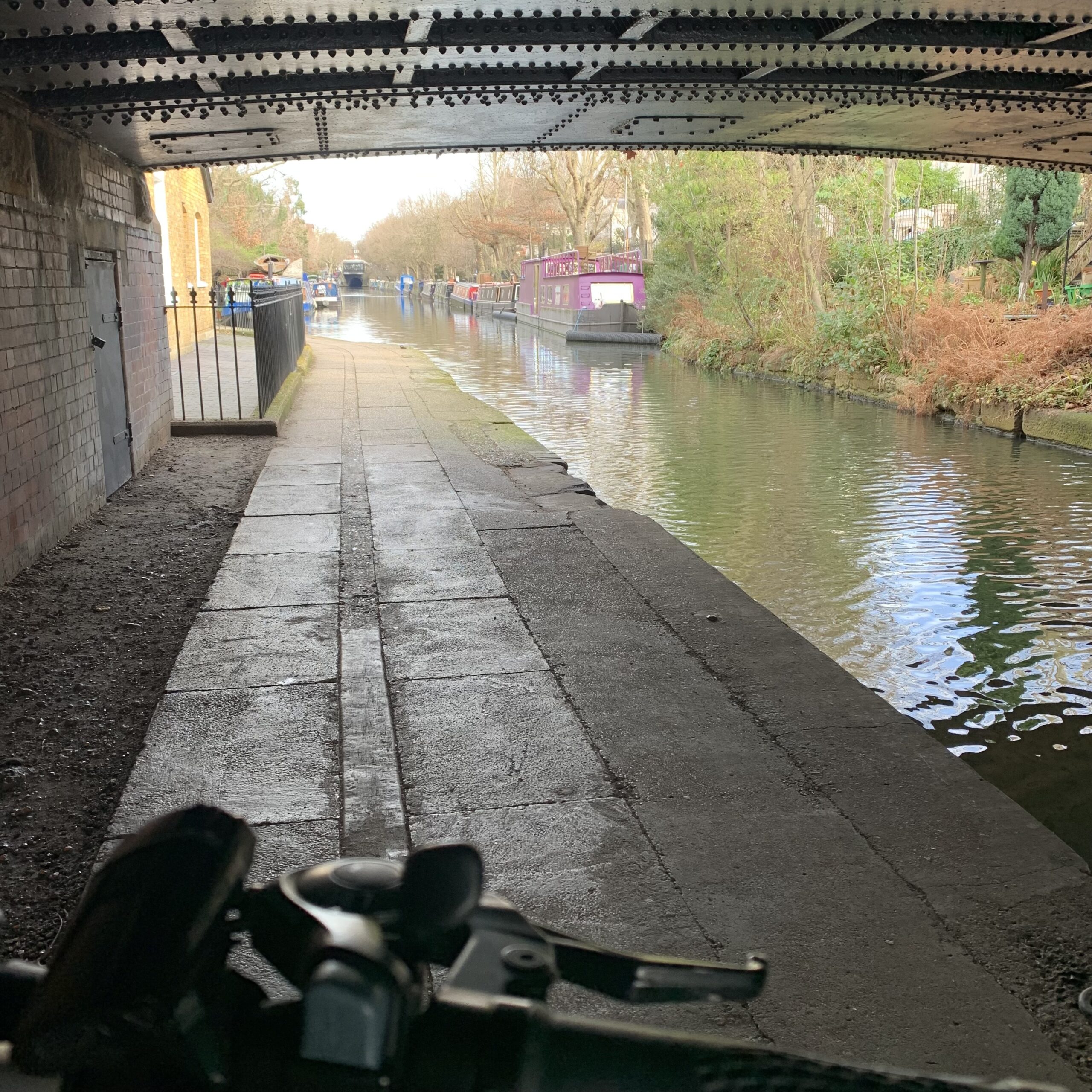 En delag gång- och cykelväg under en bro utmed en kanal i London.