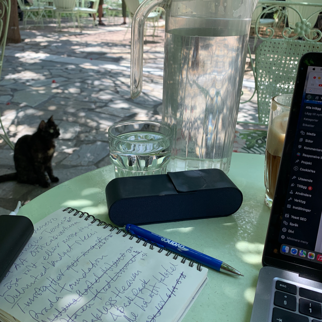 En digital nomad med sin uppslagna dator på ett cafebord, med en katt i bakgrunden i Aten i Grekland.