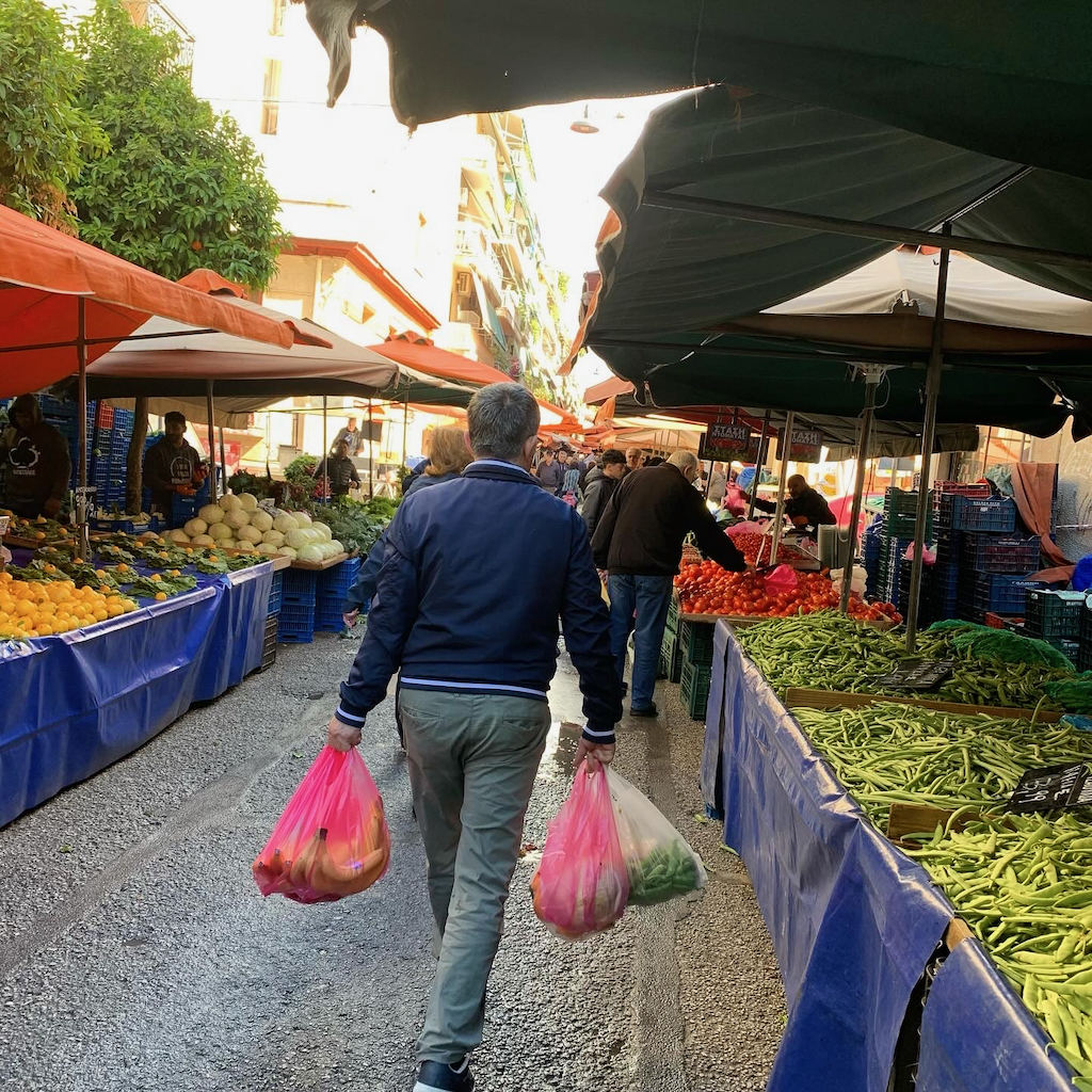 En man som bär färgglada plastkassar innehållande mat från den lokala bondens marknad i Aten.